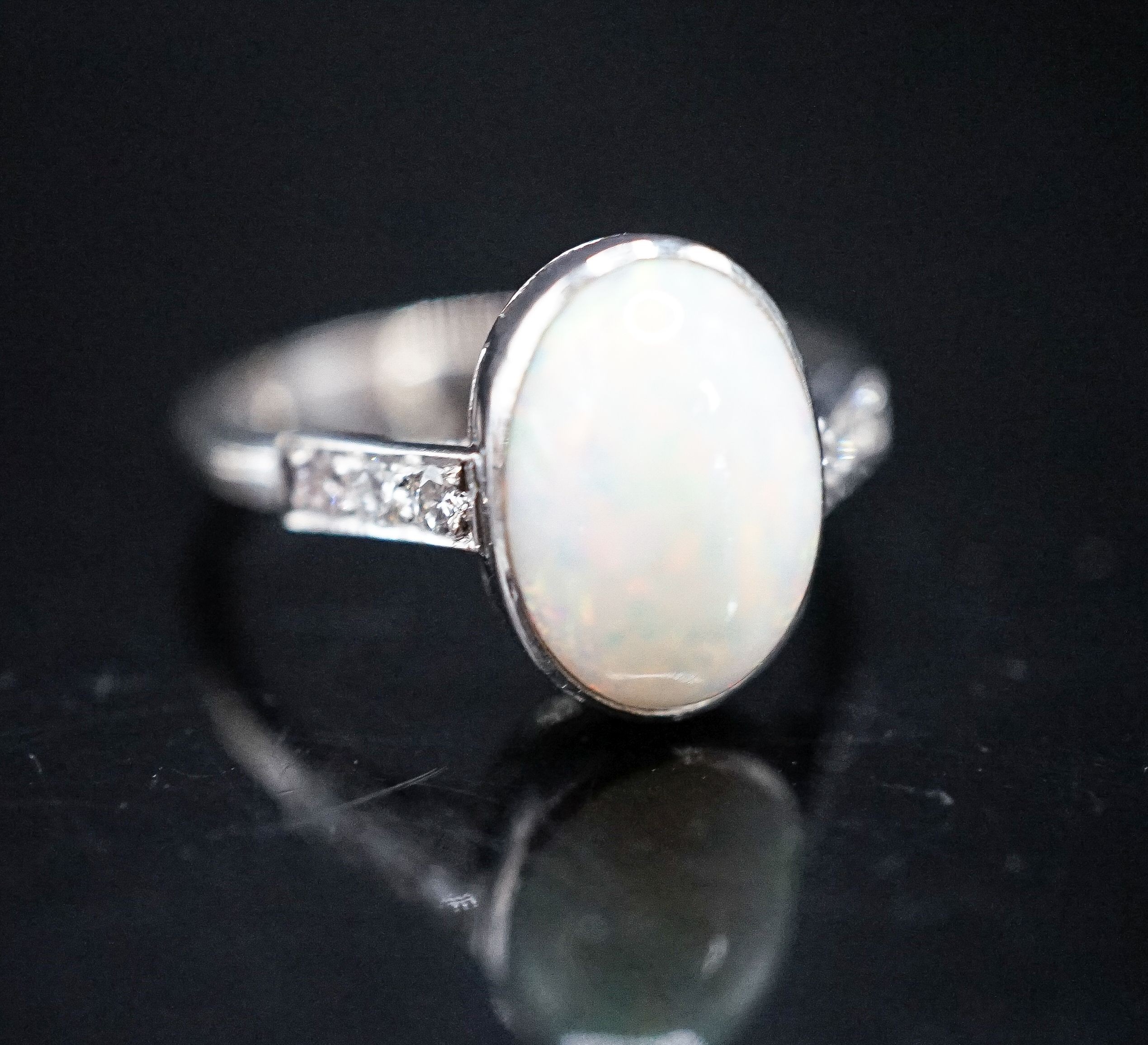 A white metal and white opal set oval ring, with diamond set shoulders, size M, gross weight 3.4 grams.